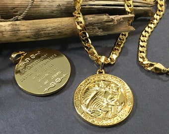 May include: Gold chain necklace with a round pendant featuring a religious image of Saint Christopher. The pendant has an inscription that reads "St Christopher patron of travelers pray for us protect us in our travels".