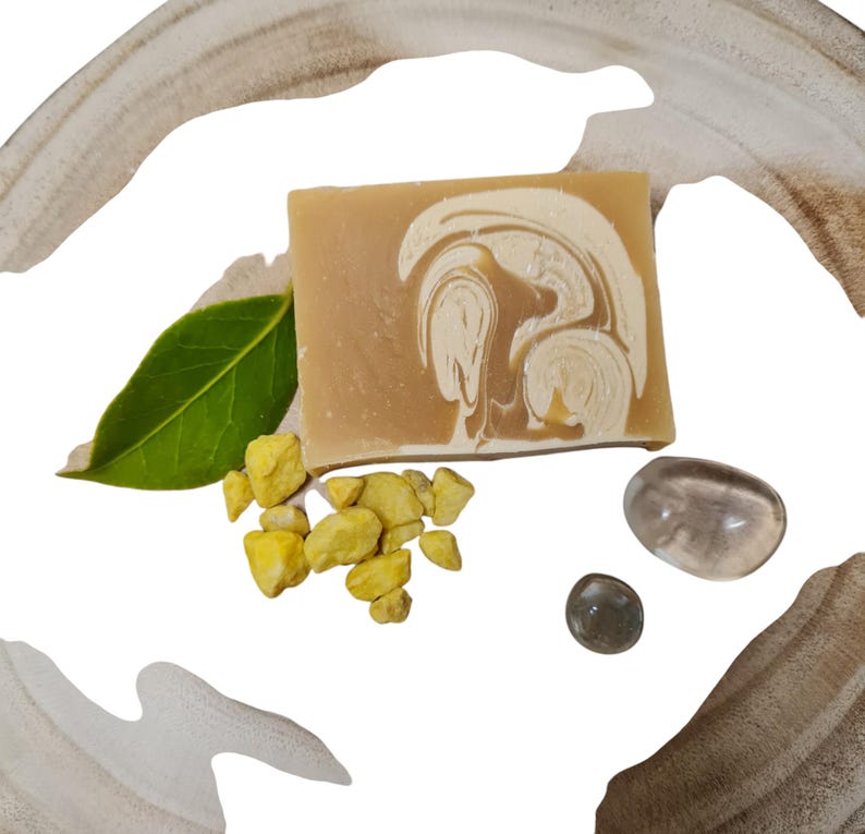 May include: A bar of handmade soap with a swirl pattern in shades of brown and white. The soap is sitting on a light brown surface with small yellow stones and clear glass stones.