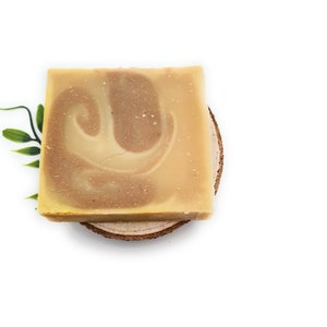 Op de afbeelding: Een rechthoekige zeep met een swirl-patroon in tinten bruin en geel. De zeep ligt op een houten schijf.