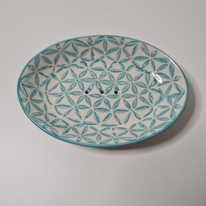 Könnte beinhalten: Eine ovale Seifenablage aus weißem Keramik mit einem blauen und rosa floralen Muster. Die Ablage hat Abflusslöcher im Boden.