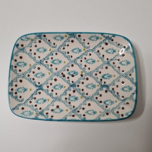 Può includere: Piatto da portata rettangolare in ceramica con base bianca, ornato da un motivo ripetuto di disegni floreali turchese e pois marroni. Il piatto ha un bordo turchese, adatto per antipasti.