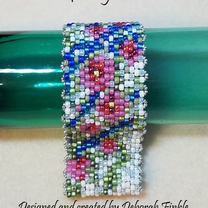 May include: A beaded bracelet with a floral pattern in shades of pink, red, blue, green, and white. The bracelet is rectangular and has a silver-colored border. Text on the image reads "Pattern for Digital Download" and "Designed and created by Deborah Finkle for Shoshin Arts 2018."