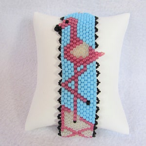 May include: A pink flamingo beaded bracelet with a blue background and black edging.