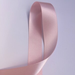 May include: A close-up of a pale pink satin ribbon. The ribbon is folded in half and the edges are visible.