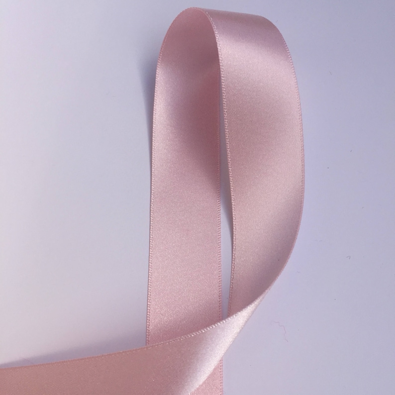 May include: A close-up of a pale pink satin ribbon. The ribbon is folded in half and the edges are visible.