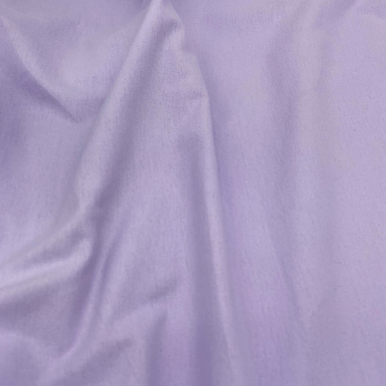 Puede incluir: Primer plano de una tela lavanda suave, con textura sutil y pliegues delicados. La tela tiene un acabado mate y parece estar drapeada, creando sombras y reflejos. La impresi&oacute;n general es de un material liso y fluido.