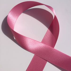 May include: A pink satin ribbon tied in a loop, a symbol of breast cancer awareness.