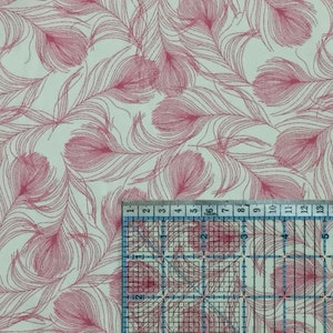 May include: A white fabric with a pink feather pattern. The fabric is measured with a ruler in inches.