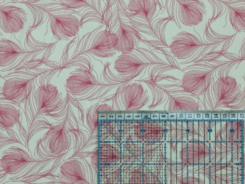 May include: A white fabric with a pink feather pattern. The fabric is measured with a ruler in inches.