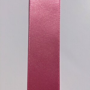 May include: A close-up of a pink satin ribbon. The ribbon has a smooth, silky texture and a subtle sheen.