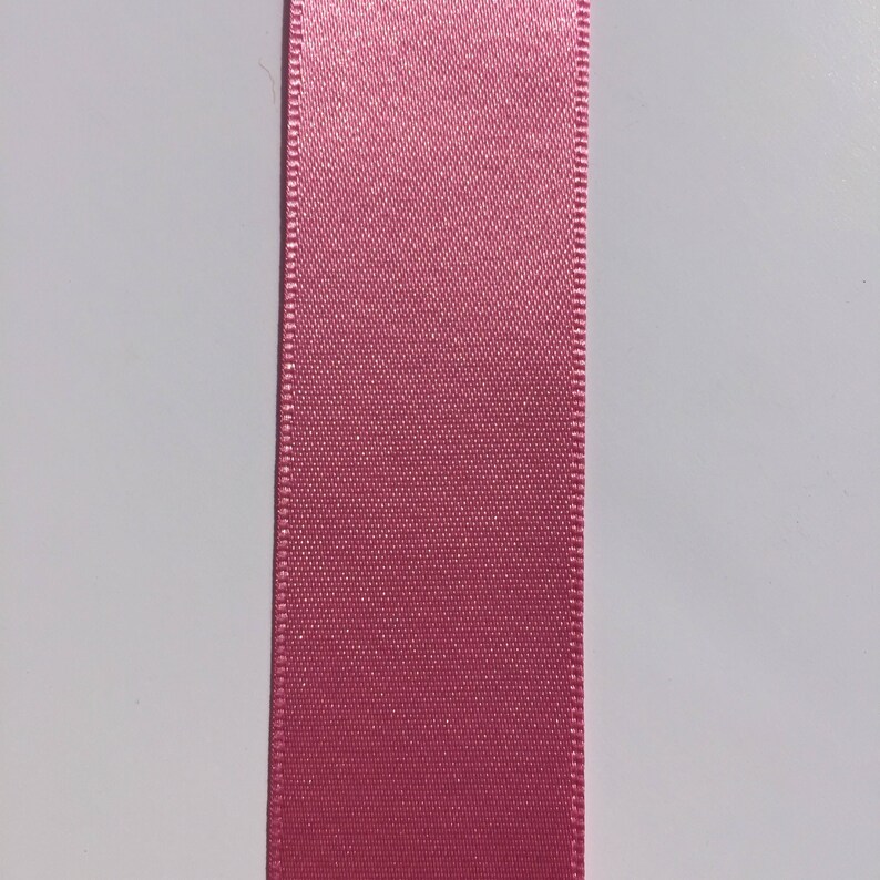 May include: A close-up of a pink satin ribbon. The ribbon has a smooth, silky texture and a subtle sheen.