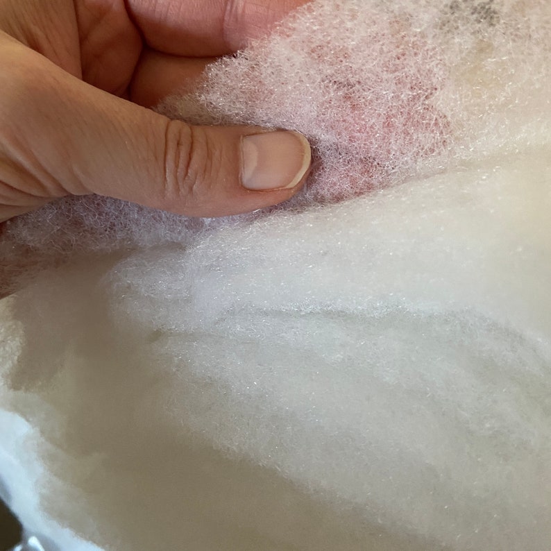 May include: Close-up of white, fluffy fiberfill stuffing. The fiberfill is soft and appears to be made of polyester.