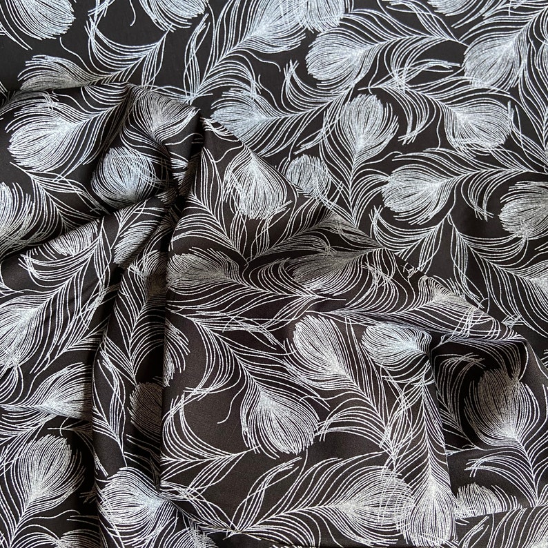 May include: Black fabric with a white feather pattern. The fabric is folded and textured.
