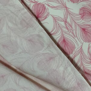May include: Two pieces of white fabric with a pink feather pattern. The fabric is folded over, showing the pattern on both sides.