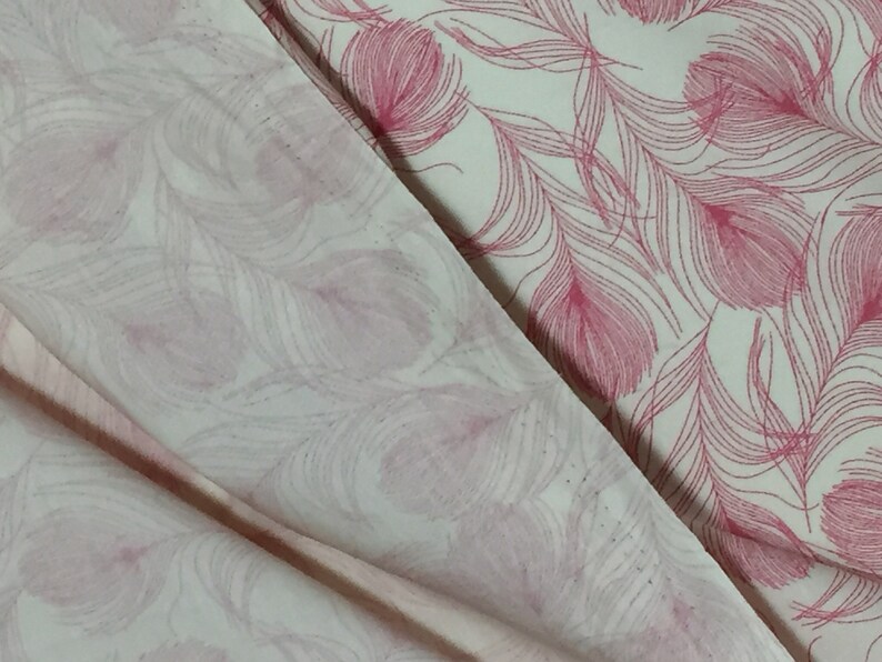 May include: Two pieces of white fabric with a pink feather pattern. The fabric is folded over, showing the pattern on both sides.