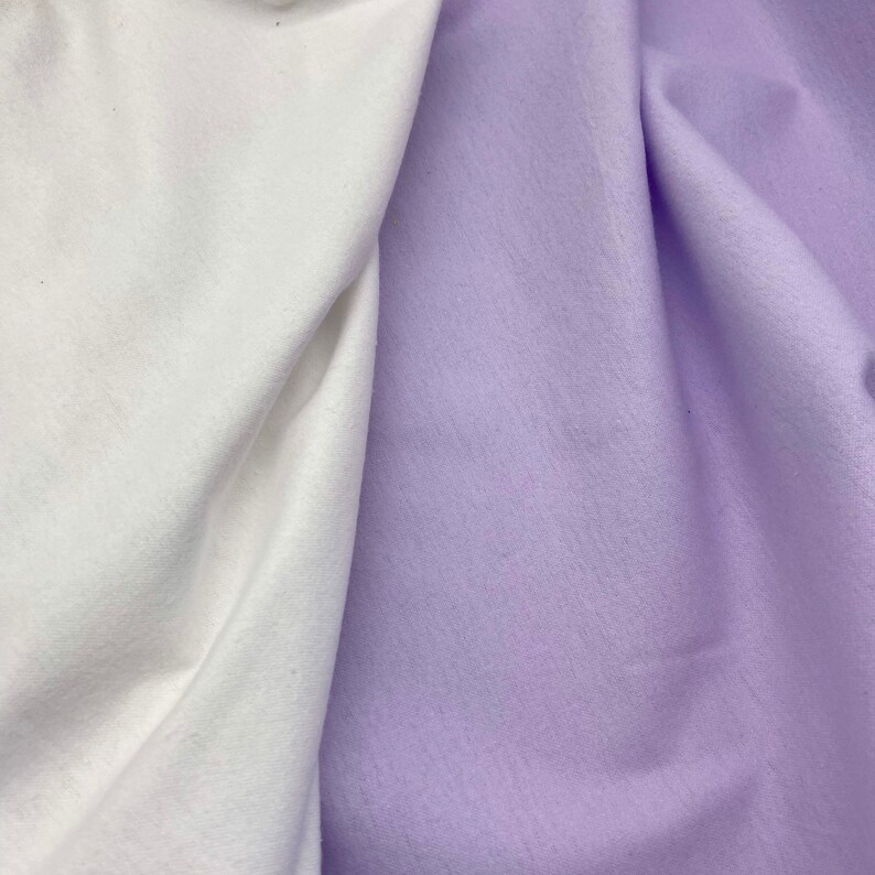 Puede incluir: Primer plano de dos muestras de tela. Una es blanca y la otra de color lavanda p&aacute;lido. Las telas est&aacute;n drapeadas, revelando su textura y pliegues. La imagen destaca el contraste entre los dos colores y las texturas.