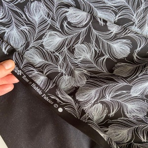 May include: Black fabric with a silver glitter feather print. The fabric has a label that reads "Rose & Hubble Fabrics".