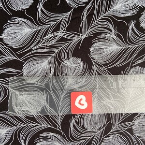 May include: Black fabric with a white feather pattern. The fabric is textured and has a subtle shimmer.