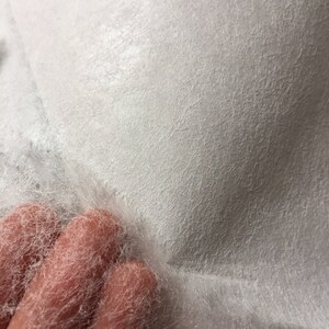 May include: White, lightweight, non-woven fabric with a textured surface. The fabric is thin and delicate, with a slightly fuzzy texture.