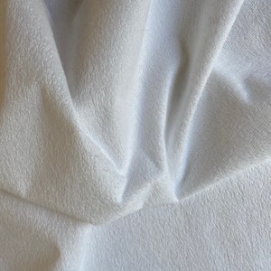 May include: White, soft, and fluffy fabric with a textured surface. The fabric is folded and draped, creating a smooth, flowing look.