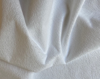 May include: White, soft, and fluffy fabric with a textured surface. The fabric is folded and draped, creating a smooth, flowing look.
