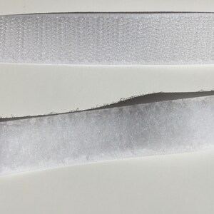 May include: Two strips of white hook and loop fastener tape. The top strip is the hook side and the bottom strip is the loop side.