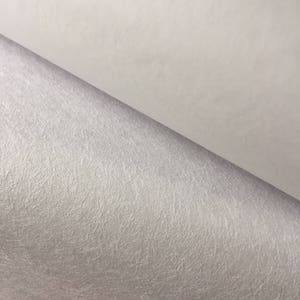 May include: Close-up of a white, textured, felt-like material. The material has a subtle sheen and a slightly grainy texture.