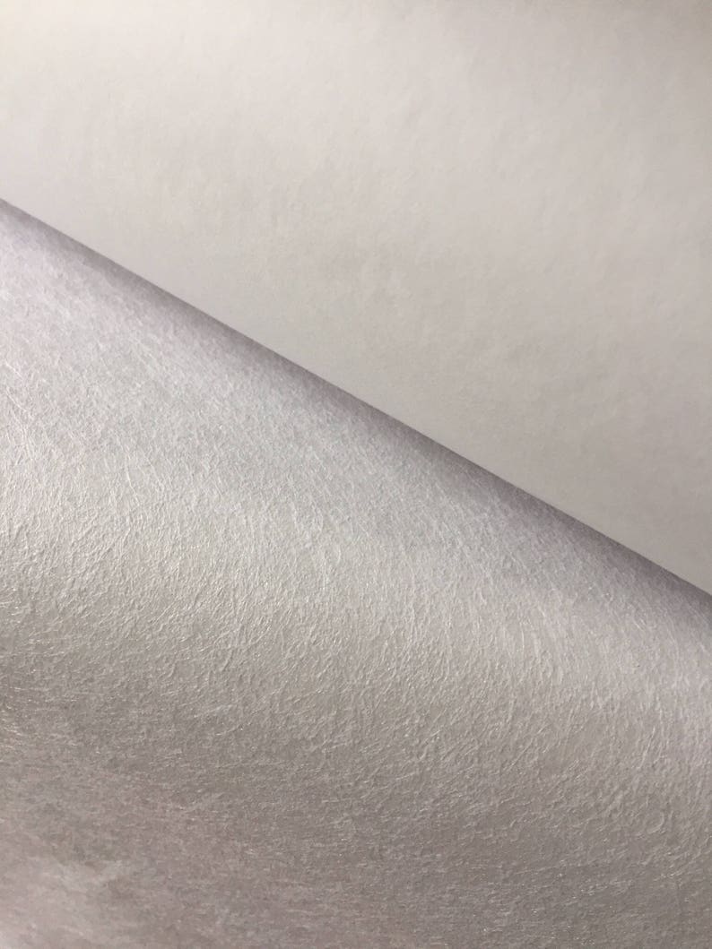 May include: Close-up of a white, textured, felt-like material. The material has a subtle sheen and a slightly grainy texture.