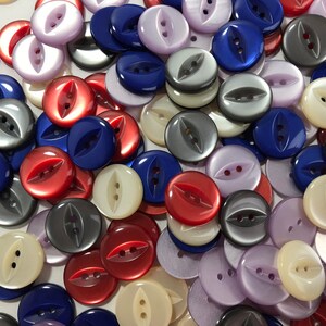 May include: A collection of two-hole buttons in various colors, including red, blue, gray, white, and purple. The buttons have a unique, slightly oval shape with a raised, leaf-like design.