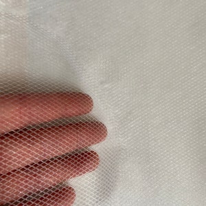 Puede incluir: Primer plano de una tela blanca y transparente con un patrón de malla en forma de diamante. La tela está sostenida por una mano, mostrando la textura y transparencia del material. La tela parece ligera y delicada.
