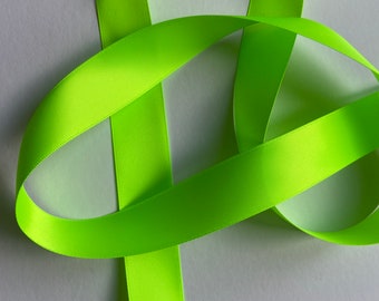 May include: A bright green satin ribbon, folded and twisted, creating a decorative loop. The ribbon is smooth and shiny, with a soft, luxurious feel.