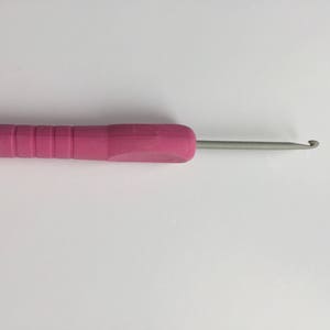Puede incluir: Un ganchillo rosa con un gancho de metal plateado. El ganchillo mide aproximadamente 15 cm de largo.