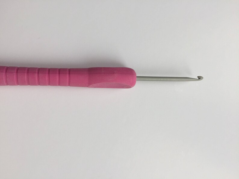 Puede incluir: Un ganchillo rosa con un gancho de metal plateado. El ganchillo mide aproximadamente 15 cm de largo.