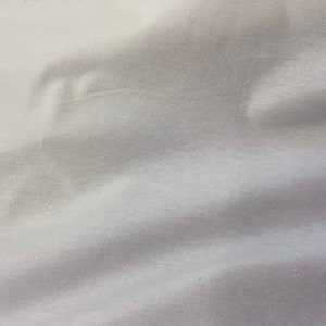 Puede incluir: Primer plano de tela blanca con pliegues suaves y sombras sutiles. La tela parece lisa y posiblemente hecha de un material ligero, creando una textura suave y fluida. La impresi&oacute;n general es de simplicidad y elegancia.