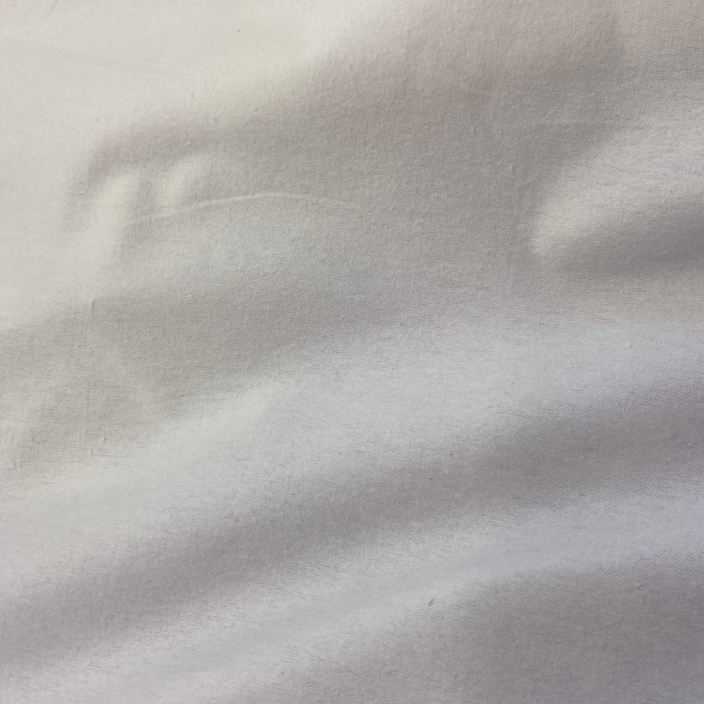 Puede incluir: Primer plano de tela blanca con pliegues suaves y sombras sutiles. La tela parece lisa y posiblemente hecha de un material ligero, creando una textura suave y fluida. La impresi&oacute;n general es de simplicidad y elegancia.