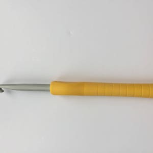 Puede incluir: Un gancho de ganchillo amarillo y plateado con un mango texturizado.