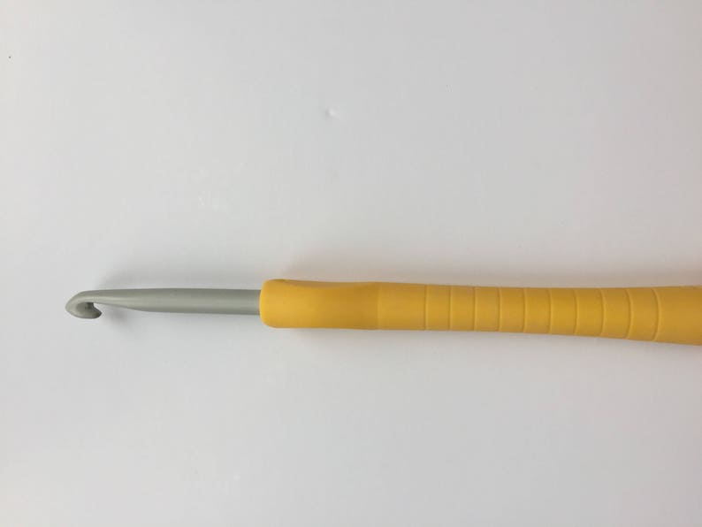 Puede incluir: Un gancho de ganchillo amarillo y plateado con un mango texturizado.