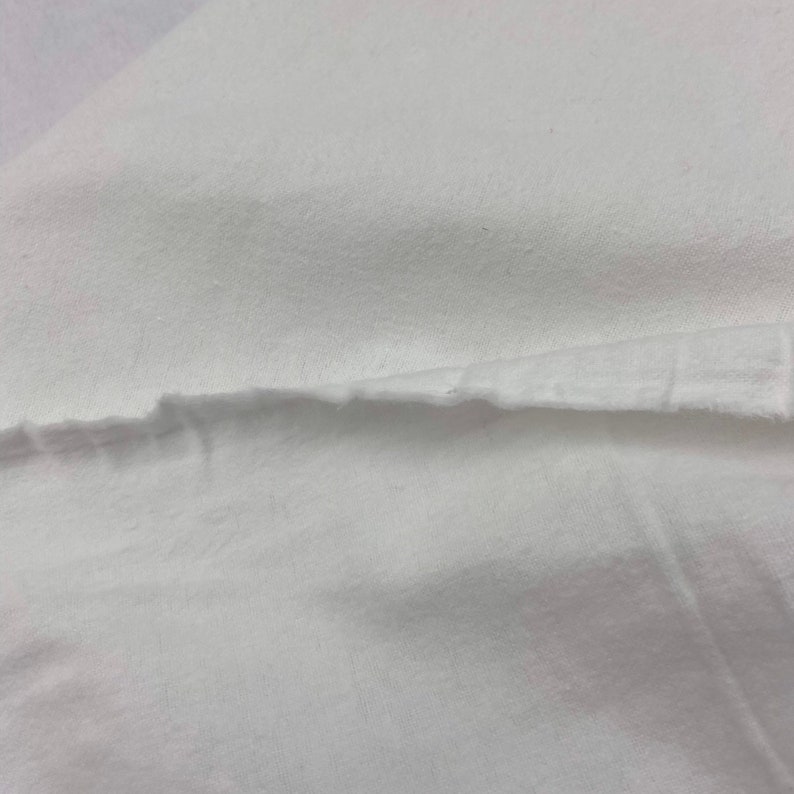 Puede incluir: Primer plano de tela blanca con borde sin rematar. La tela parece ser un material suave y tejido, posiblemente algod&oacute;n o lino. La imagen muestra la textura y la ca&iacute;da de la tela.