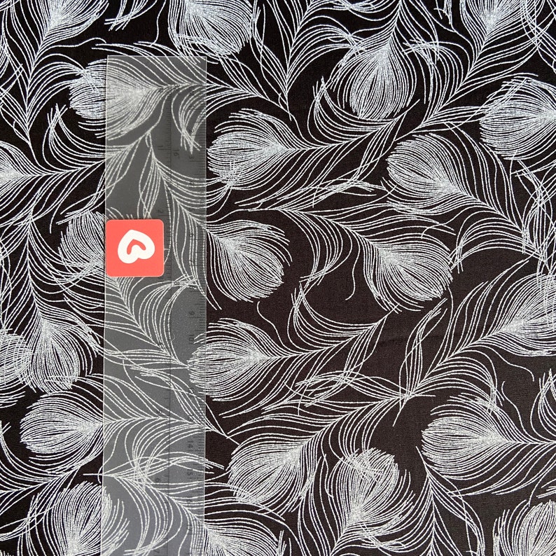 May include: Black fabric with a white feather pattern. The feathers are arranged in a random pattern and are all the same size.