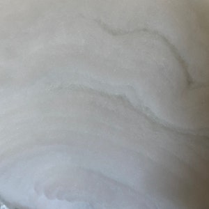 May include: Close-up of a white, textured surface with subtle gray veining. The surface has a smooth, almost velvety appearance.