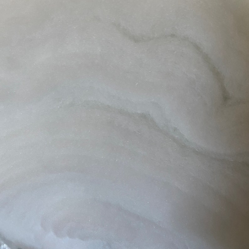 May include: Close-up of a white, textured surface with subtle gray veining. The surface has a smooth, almost velvety appearance.