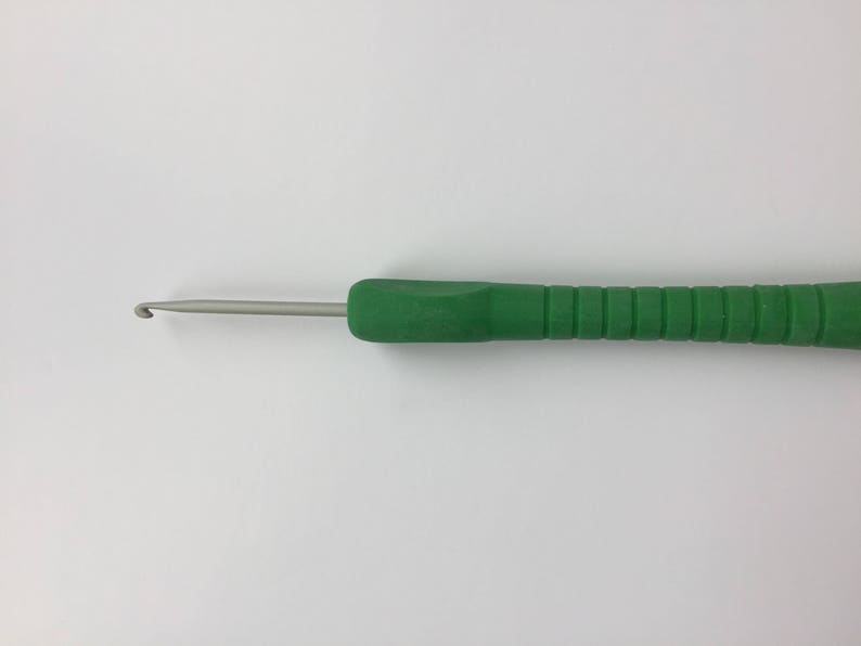 Puede incluir: Un gancho de ganchillo verde con un gancho de metal plateado.