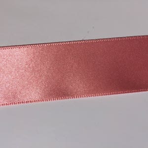 May include: A close-up of a pink satin ribbon with a stitched edge.