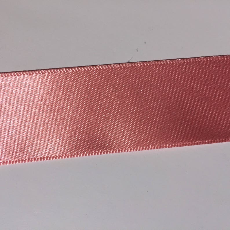 May include: A close-up of a pink satin ribbon with a stitched edge.