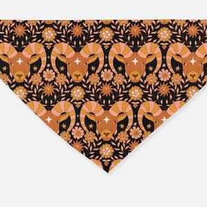 May include: Triangular bandana featuring a repeating pattern of ram heads, stars, and floral elements in shades of brown, peach, and gold on a black background. The bandana is made of a soft fabric.