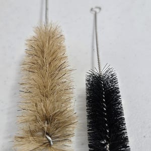 Op de afbeelding: Twee reinigingsborstels met draadhandvatten. Eén borstel heeft natuurlijke haren en de andere heeft zwarte synthetische haren.