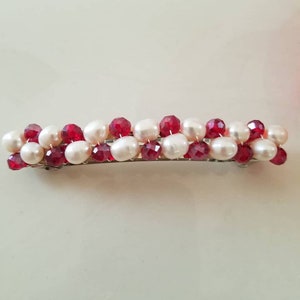 Puede incluir: Una pinza para el pelo con perlas blancas y cuentas rojas facetadas alternas.