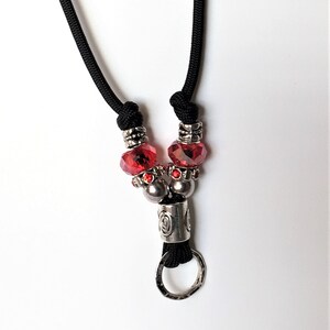 May include: A black paracord lanyard with a silver metal ring and red crystal beads.