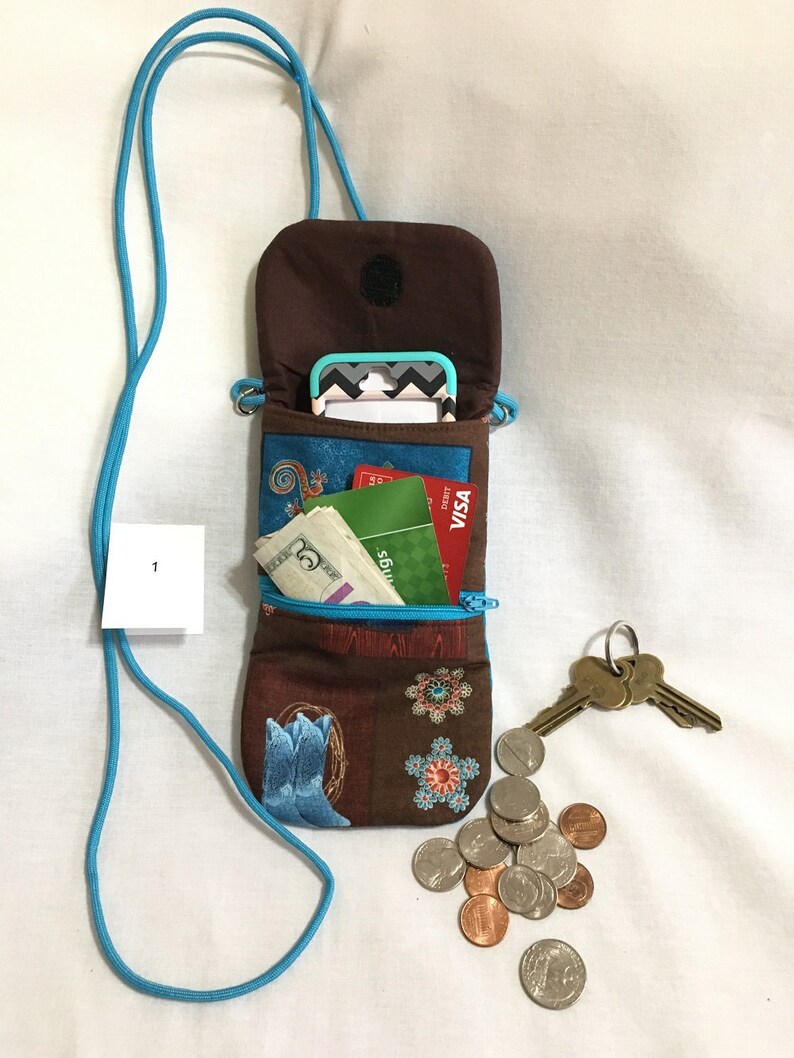 May include: A brown and blue fabric crossbody phone pouch with a zipper closure. The pouch is open and contains a mobile phone, cash, credit cards, and keys. The pouch has a turquoise strap.