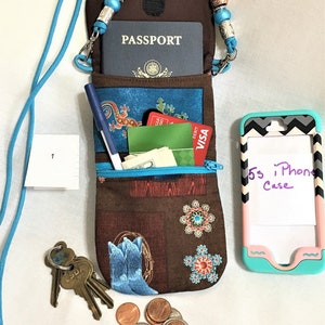 May include: A brown fabric pouch with a zipper closure and a blue and white patterned design. The pouch is hanging from a blue lanyard with silver and brown beads. The pouch is open and contains a passport, credit cards, cash, a pen, and keys. A cell phone case with the text "5s iPhone Case" is also visible.